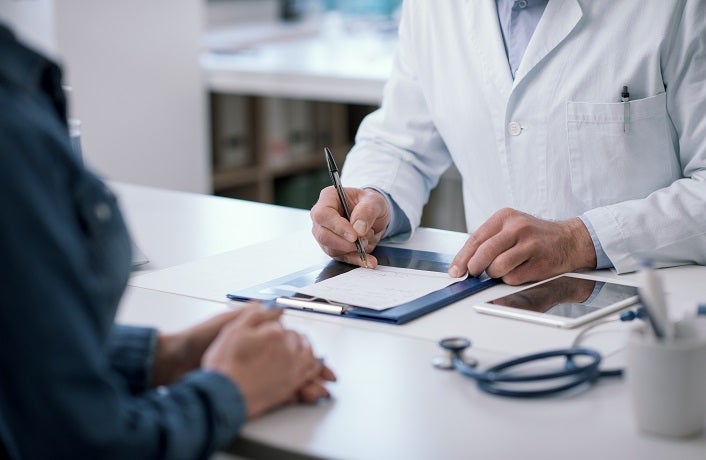 Doctor sitting at desk in his office and writing a medical prescription for his patient