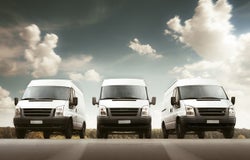 3 white delivery vans facing forward against a cloudy sky background