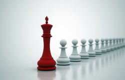 Red king chess piece in front of a row of white pawns