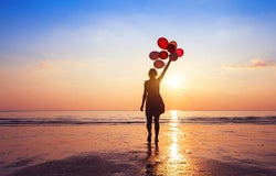 A woman on a beach holding balloons