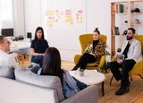 People sitting on sofas and chairs in a modern office in front of a whiteboard