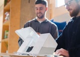 Two men standing behind and using a white POS system, including a white terminal and printer