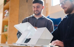 Two men standing behind and using a white POS system, including a white terminal and printer
