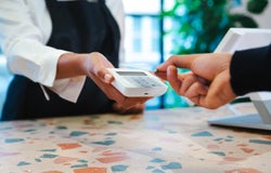 A person taps their payment card on a handheld card reader