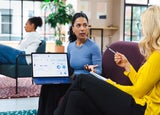 A woman shows her laptop screen to a colleague during a meeting