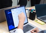 A person pointing at software on a laptop screen