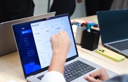 A person pointing at software on a laptop screen