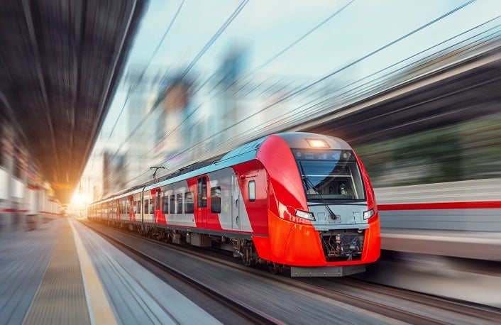 Electric passenger train drives at high speed among urban landscape.
