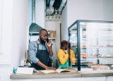 Cafe owner at a counter taking a call beside a display of baked goods