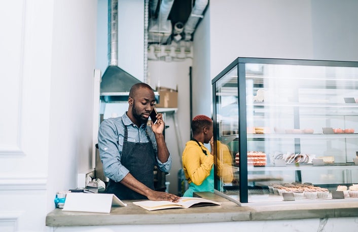Cafe owner at a counter taking a call beside a display of baked goods