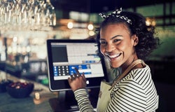 Mid shot of POS system on counter in a restaurant with female worker smiling and entering numbers