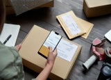 Female warehouse worker scanning barcode on shipping box on smartphone.