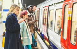 People waiting for the train at subway station. Mixed race persons, two men and two women, staying on a line and waiting to board the train. Commuting and transport