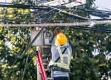 A technician on a ladder fixes a pole mounted fiber optic terminal splitter box to repair or restore internet connection to nearby houses.