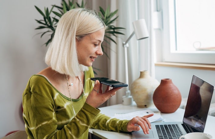 gen z female working on laptop and talking on mobile phone in her room