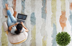 Overhead shot of a young woman working on a laptop whilst sat on a stripey multicoloured carpet