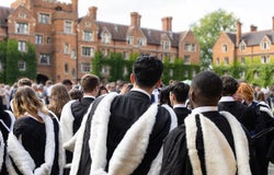 Back view of Male and female fresh graduate students with gown and academic address walk in campus of Cambridge University, UK during congregation day.