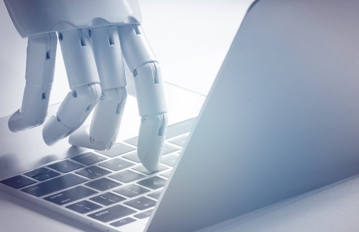 Robot hand touching a keyboard of a Mac computer about to type