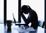Stressed business woman sits in front of a laptop at an office desk with her head in her hands