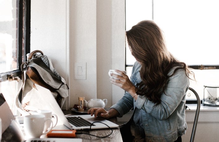 woman holding coffee cup looking at her laptop screen