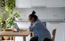 Unhappy young woman sitting at kitchen table looking at laptop having problems in job searching