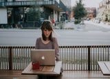 a woman works at a laptop at a roadside cafe
