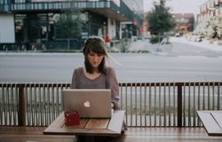 a woman works at a laptop at a roadside cafe