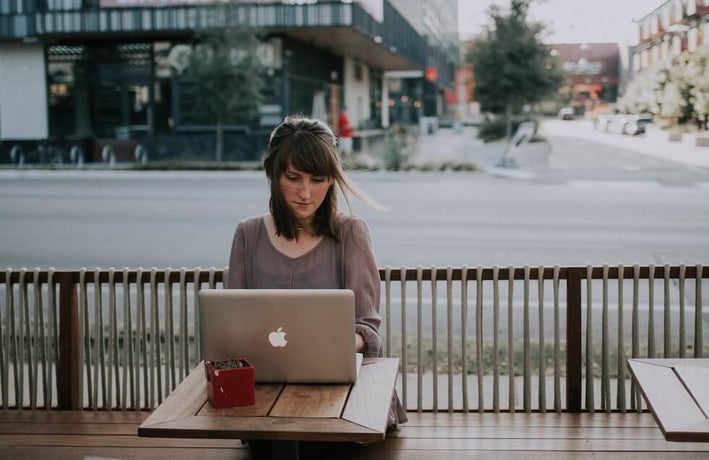 a woman works at a laptop at a roadside cafe