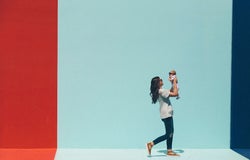 a woman holds her baby aloft against a colourful painted wall