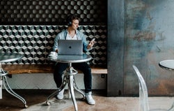 a man in a fashionable office environment working on a laptop looks at his phone