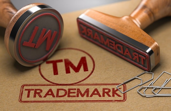 3D illustration of two rubber stamps with the word trademark and the symbol TM over brown paper background. Trade-mark Registration Concept