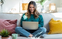 Shot of woman working with laptop while sitting on couch in living room at home