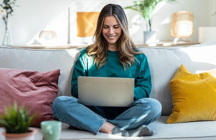 Shot of woman working with laptop while sitting on couch in living room at home