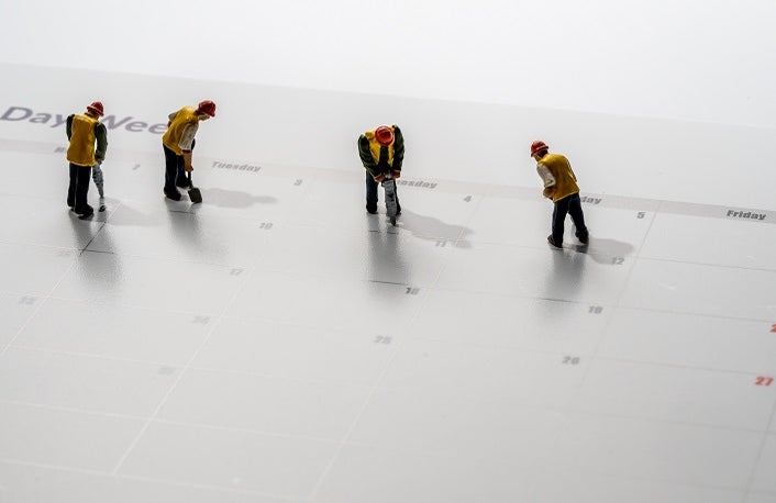 Printed calendar for a 4 day working week showing weekend days in red with small workmen working in the workweek