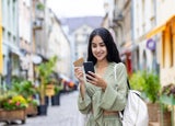 Young smiling Indian woman walking in the city, woman holding a bank credit card and phone, tourist making online booking of accommodation and booking tourist services while walking in the city.