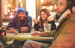 Happy friends drinking beers at trendy chalet pub restaurant in mountains on evening time - Young people having fun in winter vacation - Friendship and youth concept - Soft focus on woman face