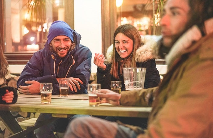 Happy friends drinking beers at trendy chalet pub restaurant in mountains on evening time - Young people having fun in winter vacation - Friendship and youth concept - Soft focus on woman face