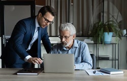 Modern tech in office. Skilled millennial ceo team leader explain work in corporate application on laptop to mature male colleague. Young man assist aged manager workmate in doing electronic paperwork