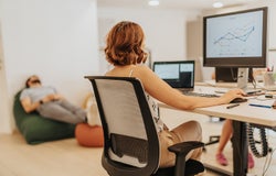Young, intelligent, business employee working on strategy, innovation, and growth in a dynamic business environment while her male coworker is taking a nap in the bag lying on lazy bag.