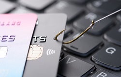 Credit card on fishing hook pulled from stack on keyboard, phishing scam data theft concept