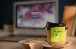 Back to Work Concept. Closeup of Welcome Note on Takeaway Coffee Cup in Office Desk. Message from a Colleague or Boss