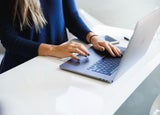 Woman's hands typing on a laptop on a white desk