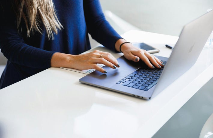 Woman's hands typing on a laptop on a white desk