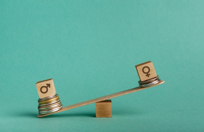 Gender pay gap. Wooden cubes with male and female gender signs on seesaw with different stacks of coins, men outweigh, copy space