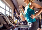 Two attractive fit women running in sports clothes on treadmills in modern gym