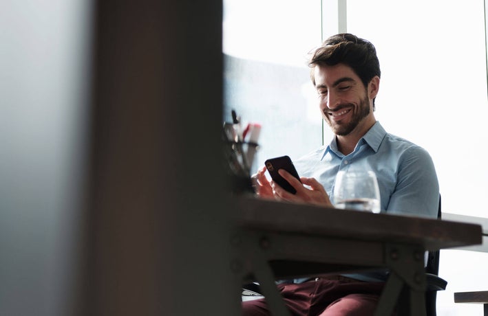 Man sitting at a desk, looking at his smartphone and smiling