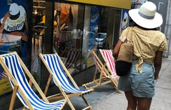 a woman wearing a hat walks past a pop up store advertised by a woman wearing a similar hat