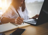 Professional doing research on a laptop and making notes
