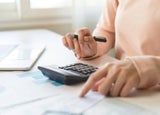 Person sitting at a desk making calculations on a calculator while holding a pen