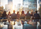 A group of employees sitting together at a meeting by a large window overlooking the city.